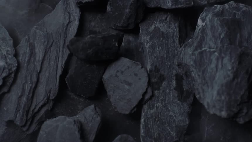 Pieces of jagged gray stone fall and break as they fall onto a pile of several other stones