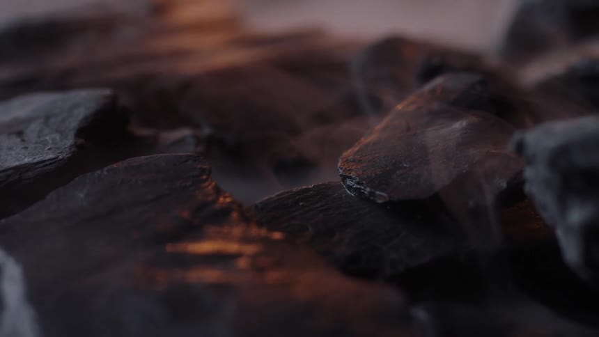 Some smoke swirls around some rocks while small flames flash around them