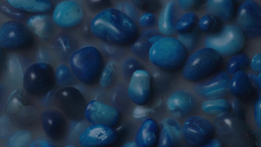 A group of smooth turquoise stones are shown sitting in a gray murky substance with smoke coming off of them
