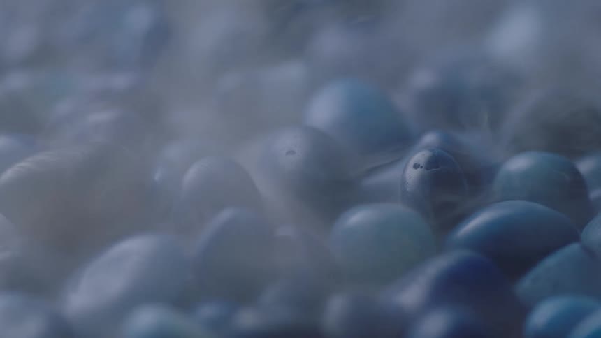 Pale vapor flows across blue pebbles before blowing away