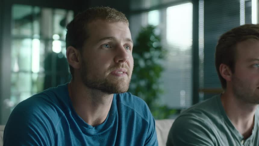 A pair of men play video games together while sitting on a sofa during the day