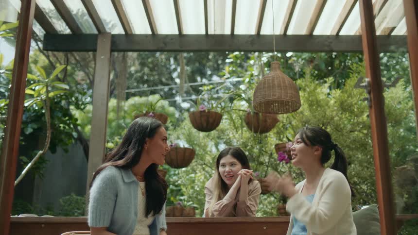 Three women sitting outside under a pergola talking and smiling