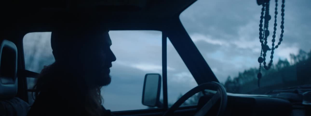 Young man with long hair and beanie driving at sundown along rural highway