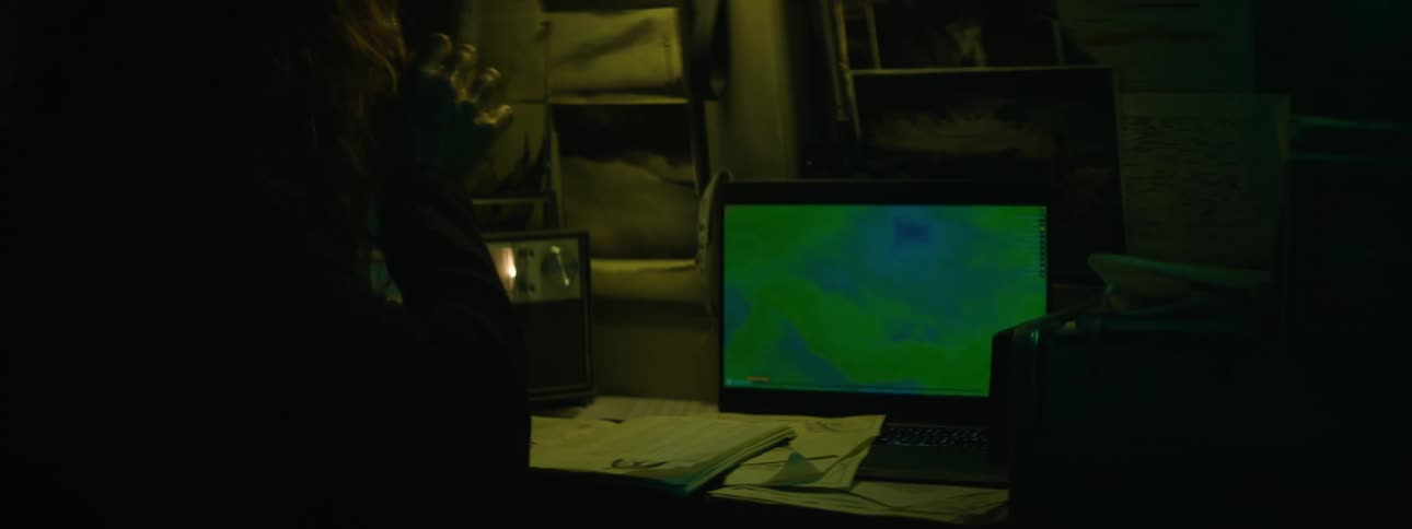 A person sitting at a desk at nighttime monitoring several machines collecting data and handwriting it