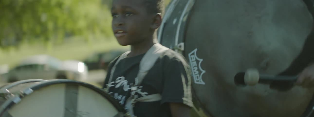 Children are playing drums and walking around in the grass