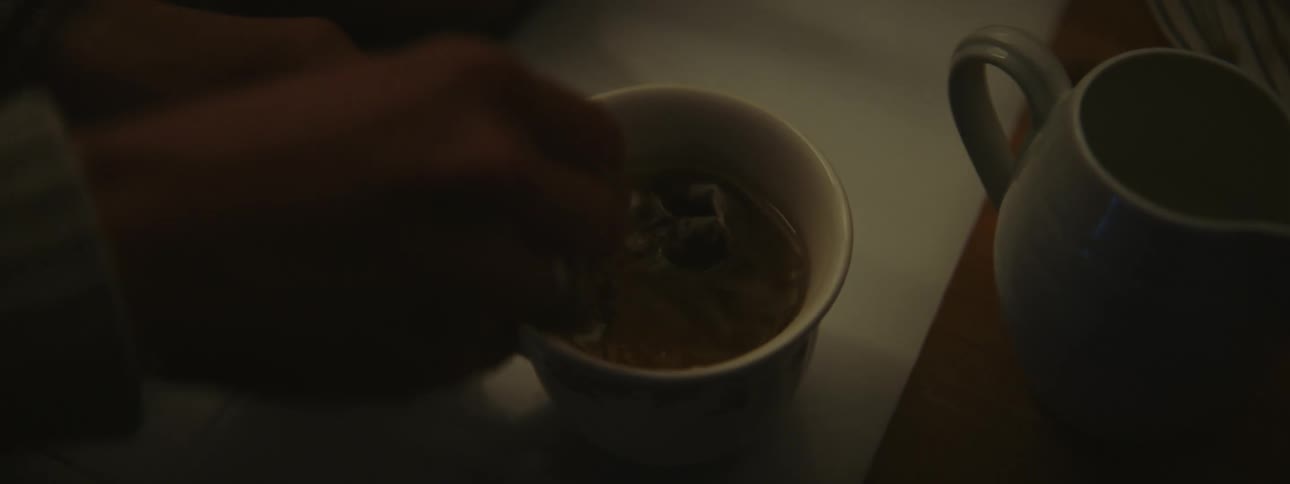 A womans hand is shown pouring tea from a kettle into a teacup stirring it and taking out the teabag