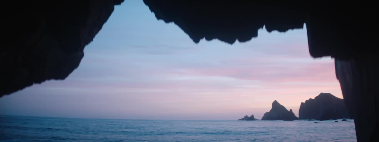 A view from a cave looking out at the ocean against a pink and blue dusk sky