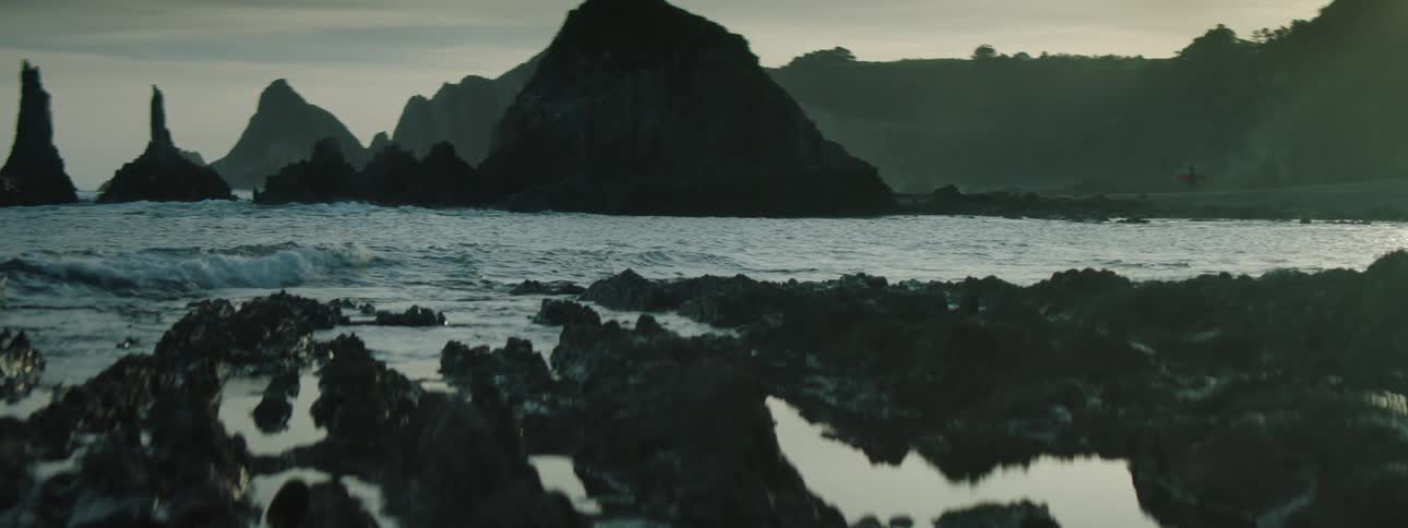 Gentle waves crashing on the rocks in the coast of a beach next to large promontories at evening