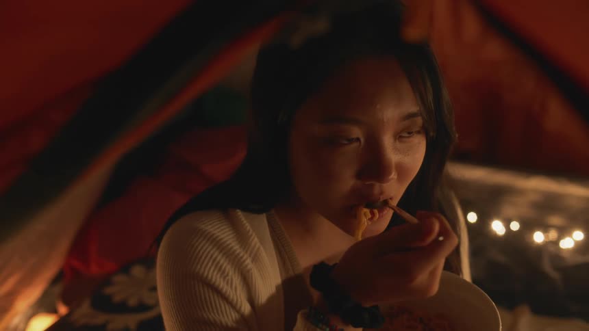 Young girl eating a bowl of noodles and laughing with friends at nighttime