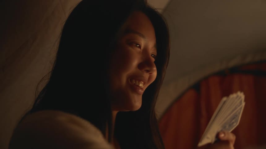 Close up of a young woman playing cards with a friend in a dimly lit room