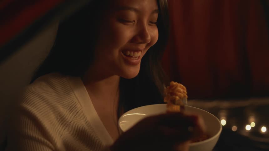 A bowl full of noodles as a woman eats them with a fork