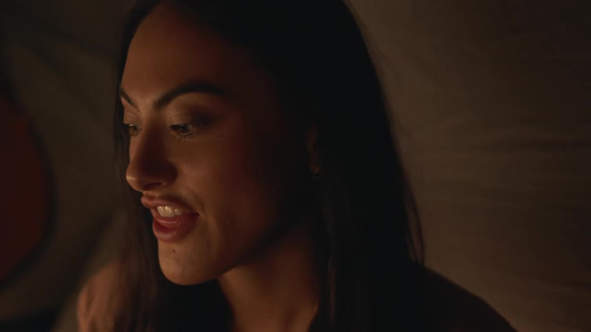 Woman with straight hair and necklace talks to person in tent