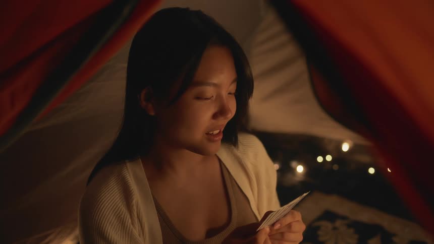 A woman sitting holding playing cards in a tent looking up and talking