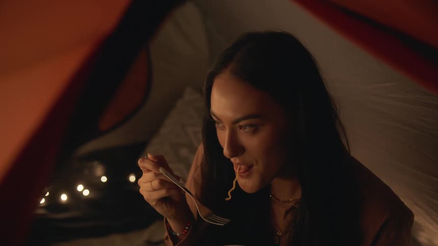 A woman laughing and smiling and then eating noodles while nodding at someone