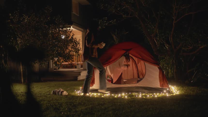 Two teenage girls are carrying bowls through the yard and into a tent at night
