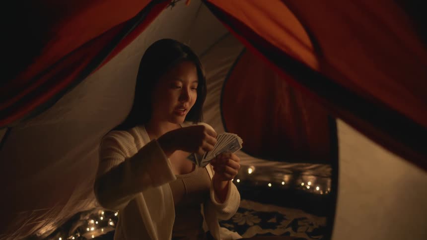 A woman is sitting alone inside of a large tent organizing a hand of playing cards