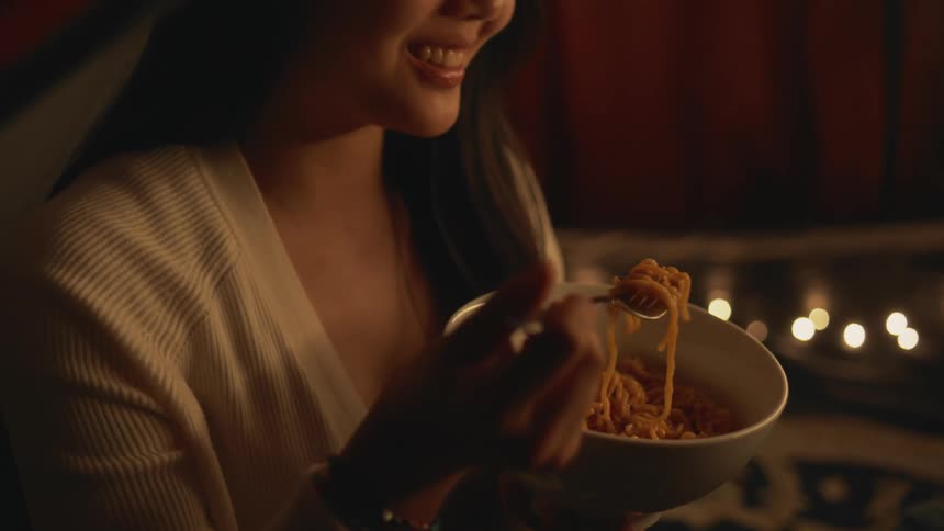 Woman sits eating noodles from white bowl with a smile