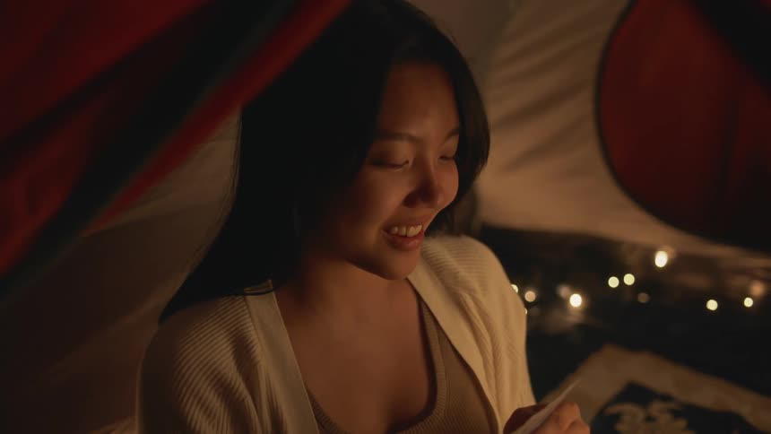 Woman with straight hair and white shirt plays card game in tent at night