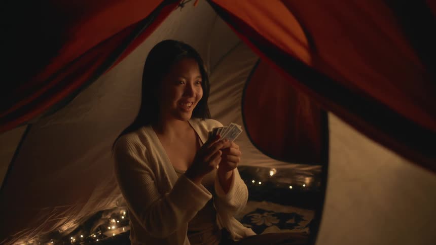 A woman sitting in a tent holding playing cards smiling and laughing