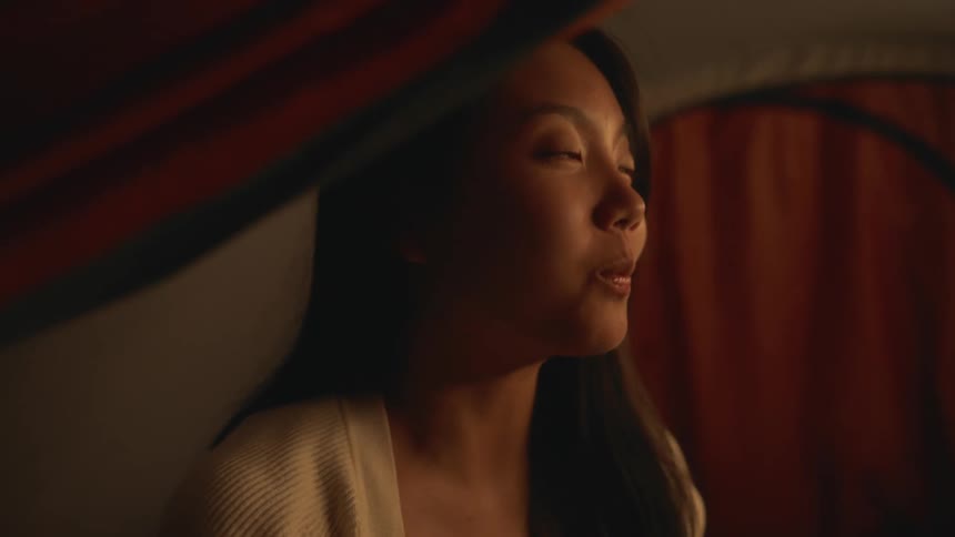 Young woman sitting in a tent and eating noodles while engaging with a friend