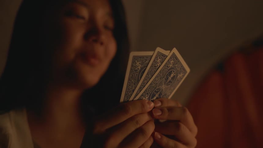 Young woman sitting inside a tent holding a hand of cards smiling discards two