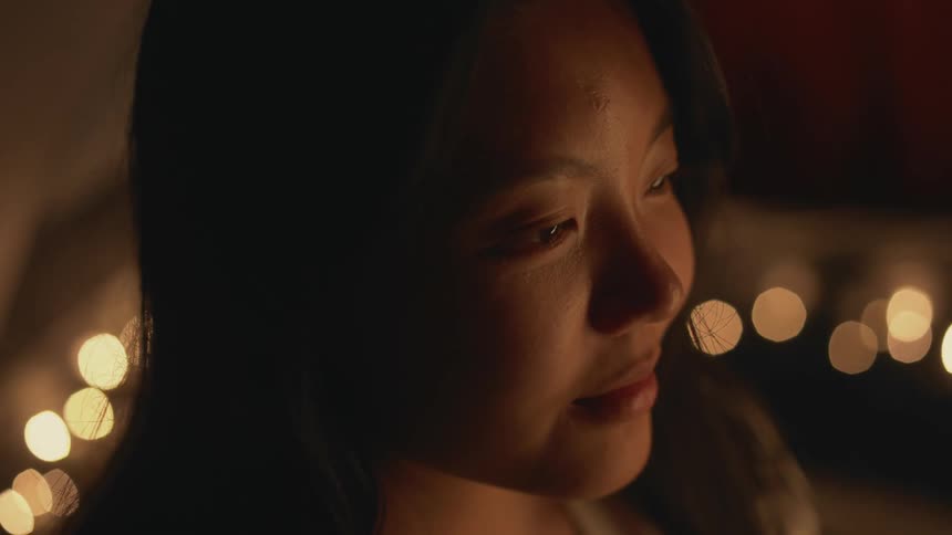 Close up of a girl surrounded by candles on a dimly lit room opens her eyes