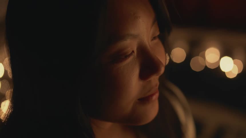 Close up of a girl surrounded by candles on a dimly lit room opening her eyes