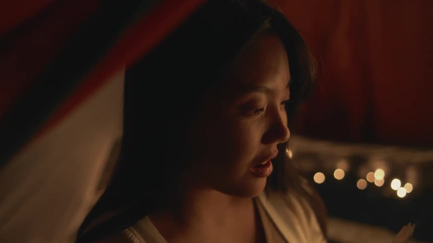 Young woman sitting in a tent at nighttime having a conversation with someone smiling and laughing