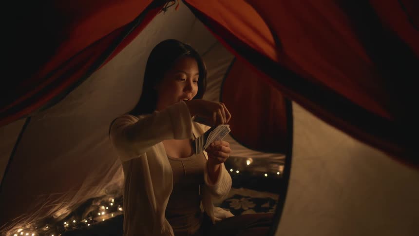 A young woman is inside of her tent and is playing cards
