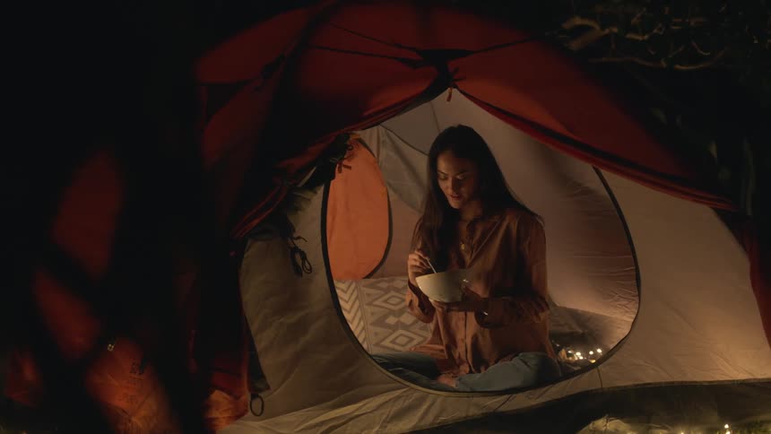 A woman is eating food while sitting in her tent