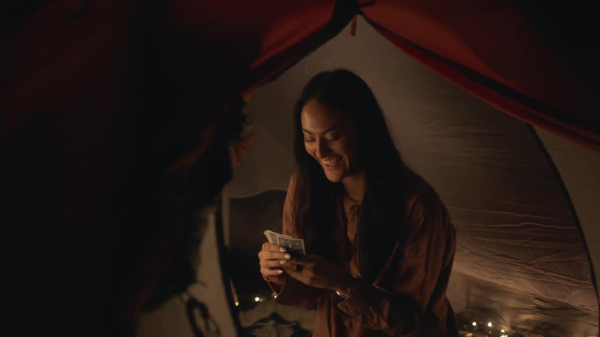 A woman sitting in a tent holding cards in her hands laughing and smiling as she puts a card down