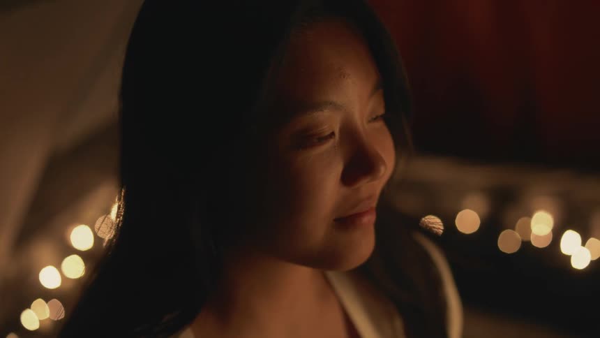 Close up of a girl surrounded by candles on a dimly lit room opening her eyes