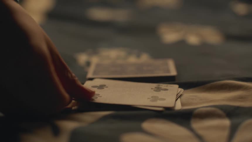 A persons hand is seen laying playing cards on a tablecloth