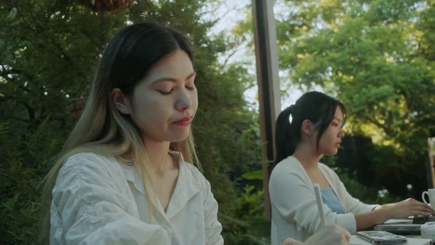 Young woman working with friends on a table in the garden drawing on a tablet with a stylus