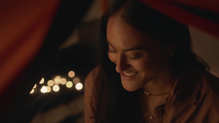 A woman sitting inside of a tent talks to someone off camera and smiles