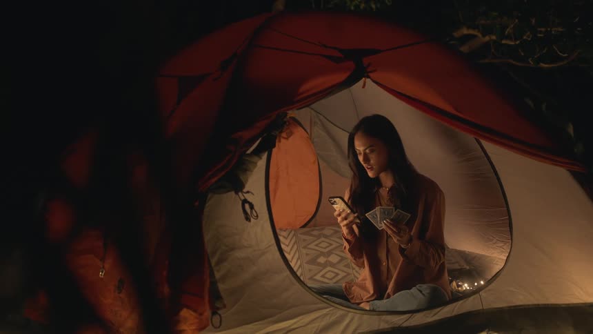A woman sitting in a tent holding playing cards looking at her cellphone