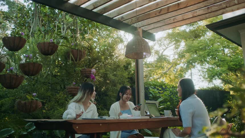 Asian women sit at a picnic table and converse happily while working
