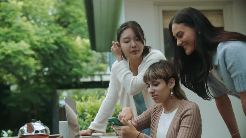 Women huddle sharing smartphone screen on patio near house