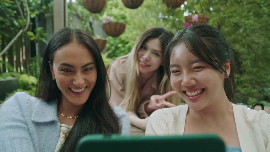 Three women looking at a phone in ones hand smiling and posing