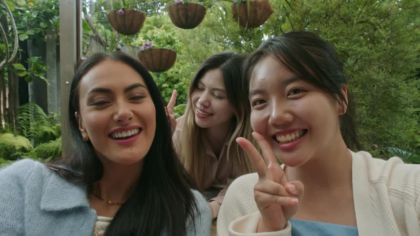 Three women sitting outside smiling and posing for a camera