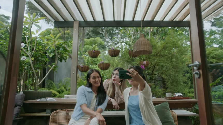 A group of women pose for a selfie while sitting together on a patio during the day