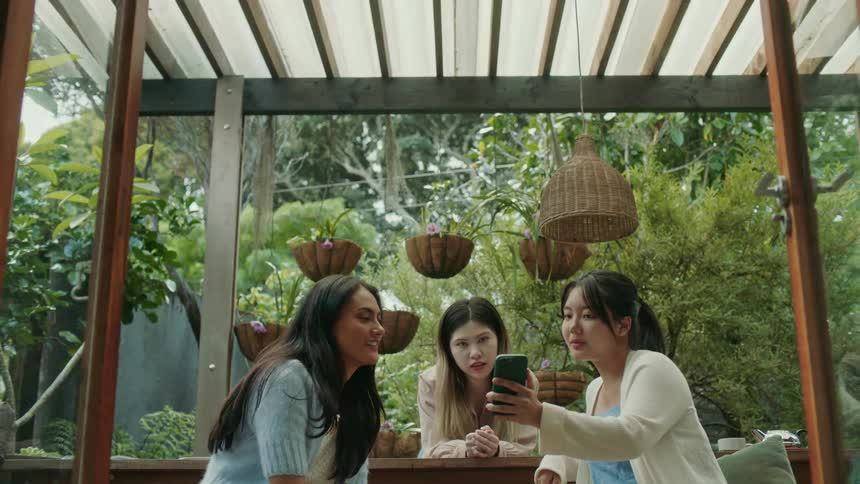 Three women sitting around a table outside all looking at a phone in the one womans hand