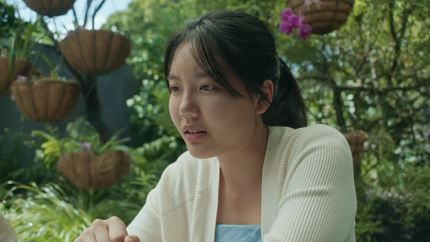 A teenage girl is sitting outside at a table working on a laptop computer as another girl sits next to her