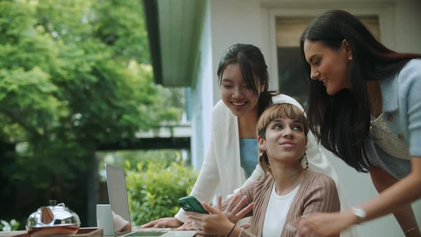 Friends sitting at a table in the backyard talk white looking at a phone