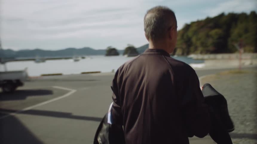 A man walking while carrying a wet suit and setting it down on a concrete sidewalk