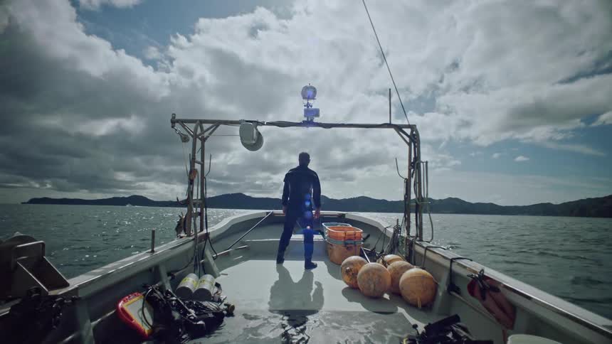 A man standing on a moving boat facing forward looking out over the water