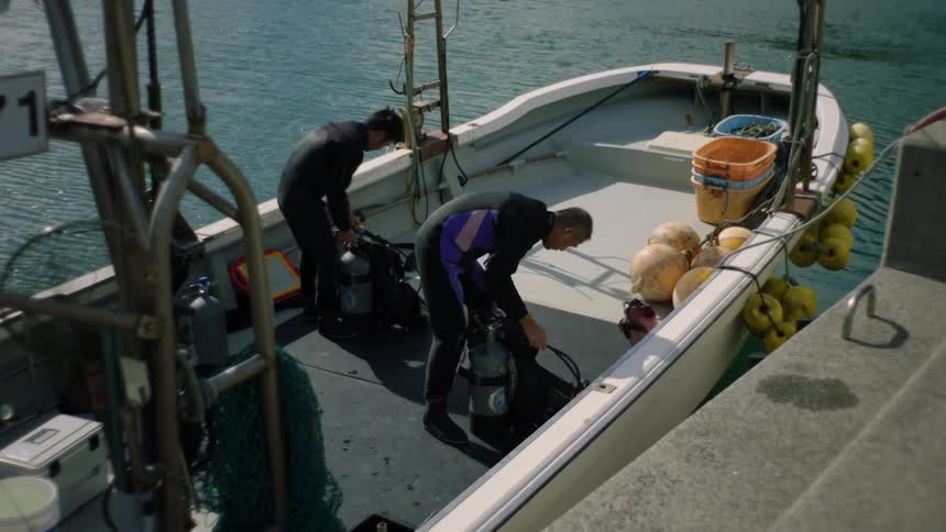 Two men in a boat hunched over preparing scuba tanks