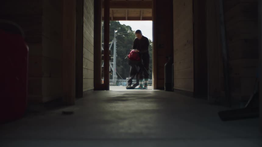 A man standing in a doorway manipulating a wetsuit and starting to put it on