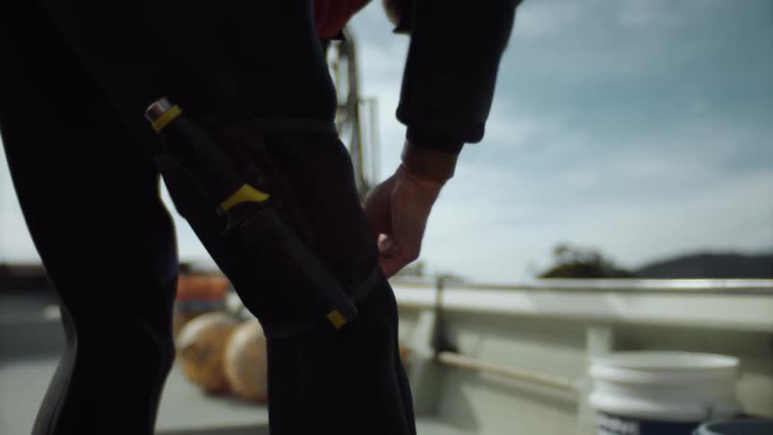 A man on a boat putting a suit and gear on