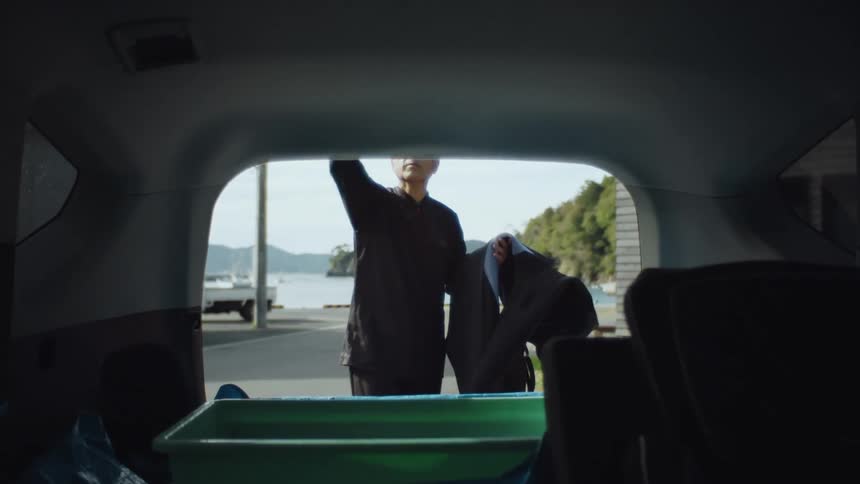 A man opens the back of his van and takes a scuba diving suit from a container inside the vehicle
